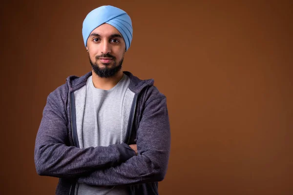 Jovem barbudo indiana sikh homem vestindo turbante contra marrom backg — Fotografia de Stock