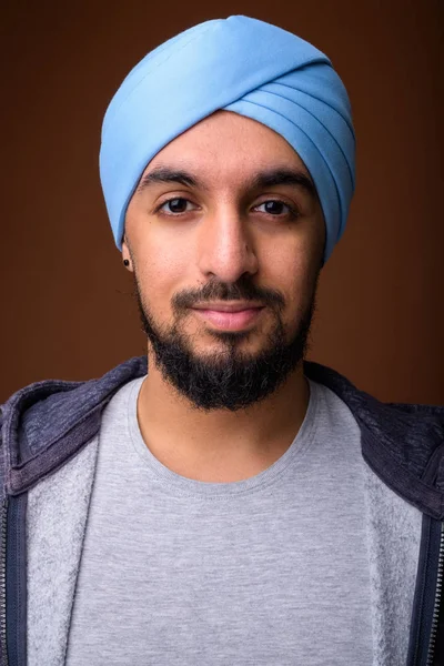 Jonge bebaarde Indiase Sikh man draagt tulband tegen bruine rug — Stockfoto