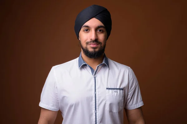 Joven barbudo hombre Sikh indio usando turbante contra respaldo marrón — Foto de Stock