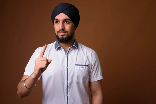 Young bearded Indian Sikh man wearing turban against brown backg — 스톡 사진