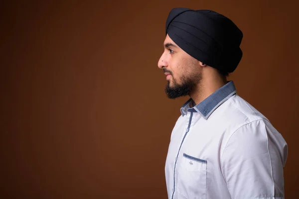 Ung skäggig indisk sikh man bär turban mot brun rygg — Stockfoto