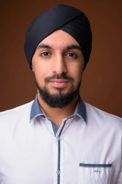 Young bearded Indian Sikh man wearing turban against brown backg — Stock Photo, Image