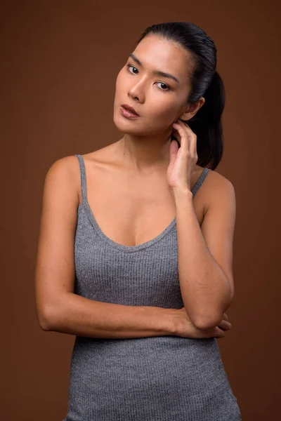 Studiová střela z krásné asijské ženy proti hnědým pozadím — Stock fotografie