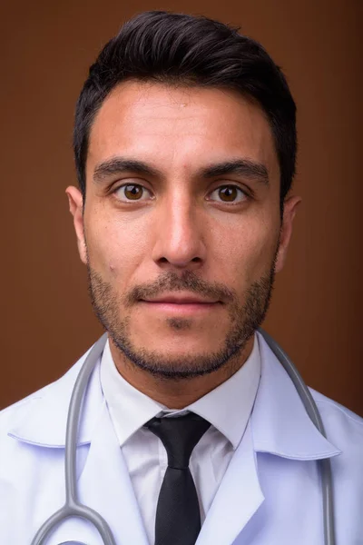 Junger hübscher hispanischer Arzt vor braunem Hintergrund — Stockfoto