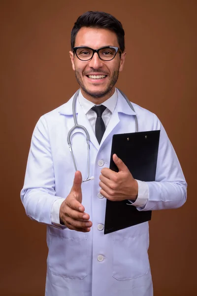 Jovem bonito homem hispânico médico contra fundo marrom — Fotografia de Stock