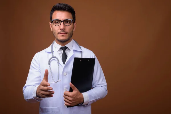 Jovem bonito homem hispânico médico contra fundo marrom — Fotografia de Stock