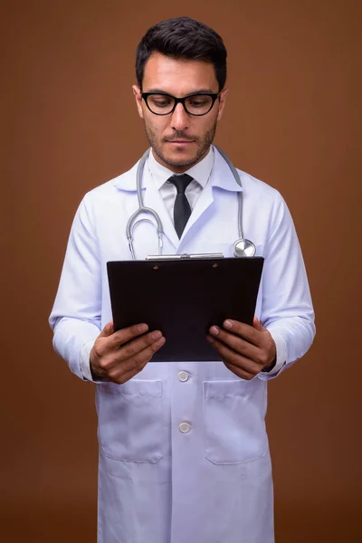 Young handsome Hispanic man doctor against brown background — Stock Photo, Image