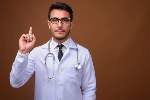 Joven guapo hispano hombre doctor contra marrón fondo — Foto de Stock