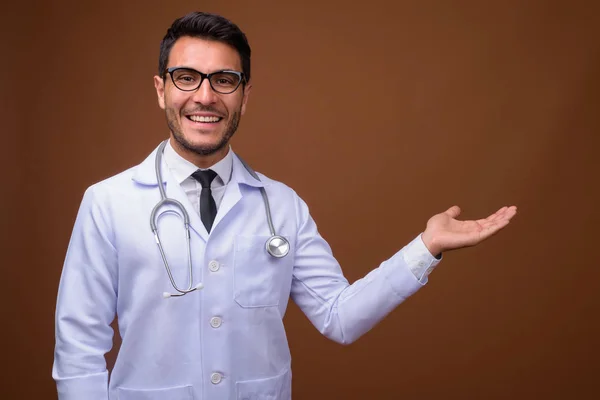 Fiatal jóképű spanyol férfi orvos barna háttér — Stock Fotó
