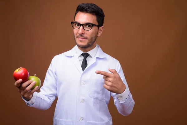 Jovem bonito homem hispânico médico contra fundo marrom — Fotografia de Stock