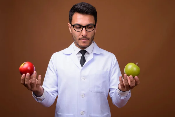 Joven guapo hispano hombre doctor contra marrón fondo —  Fotos de Stock