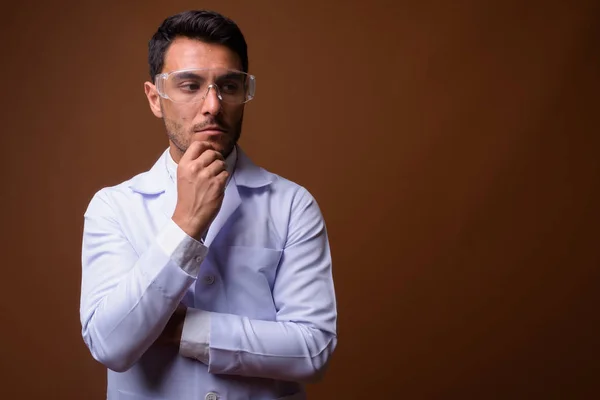 Junger hübscher hispanischer Arzt vor braunem Hintergrund — Stockfoto