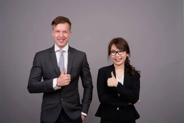 Jonge zakenman en jong Aziatisch zakenvrouw tegen grijs bac — Stockfoto