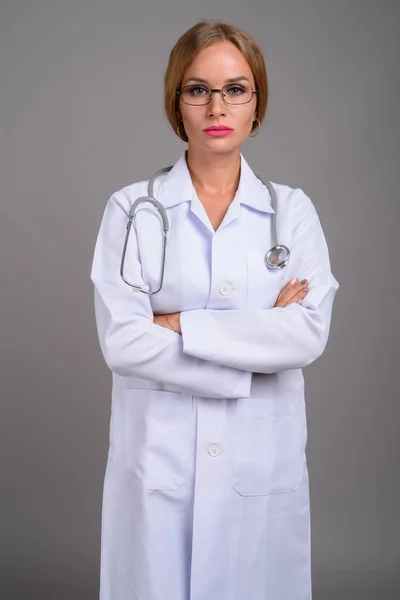 Joven hermosa mujer médico con cabello rubio contra gris backgr —  Fotos de Stock