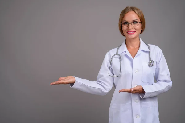 Joven hermosa mujer médico con cabello rubio contra gris backgr — Foto de Stock