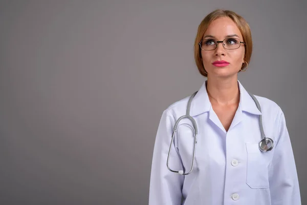 Jovem médico mulher bonita com cabelo loiro contra backgr cinza — Fotografia de Stock