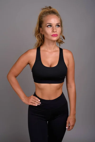 Junge schöne Frau mit blonden Haaren bereit für das Fitnessstudio gegen grau — Stockfoto