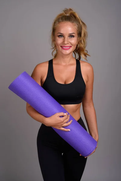 Jovem mulher bonita com cabelo loiro pronto para ginásio contra cinza — Fotografia de Stock