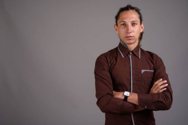 Studio shot of young man with dreadlocks wearing brown shirt against gray background