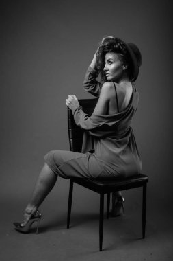 Studio shot of young beautiful woman with curly hair posing against gray background in black and white