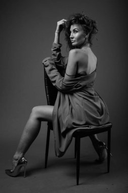 Studio shot of young beautiful woman with curly hair posing against gray background in black and white