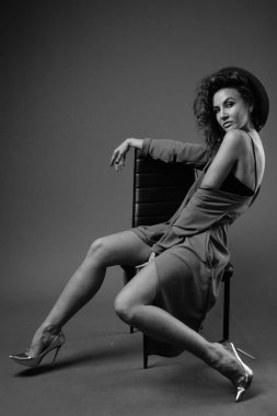 Studio shot of young beautiful woman with curly hair posing against gray background in black and white