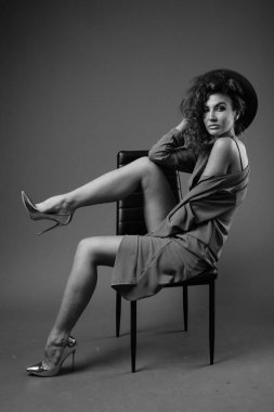 Studio shot of young beautiful woman with curly hair posing against gray background in black and white