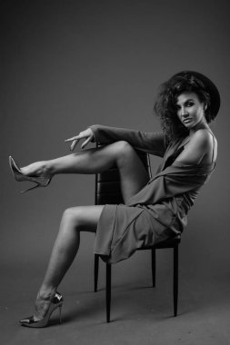 Studio shot of young beautiful woman with curly hair posing against gray background in black and white