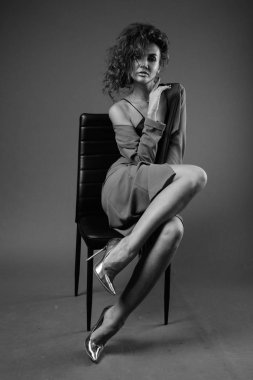 Studio shot of young beautiful woman with curly hair posing against gray background in black and white