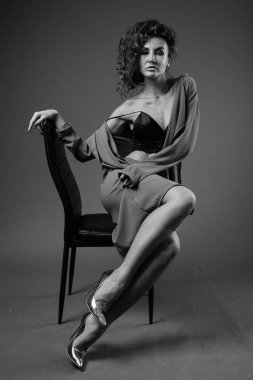 Studio shot of young beautiful woman with curly hair posing against gray background in black and white