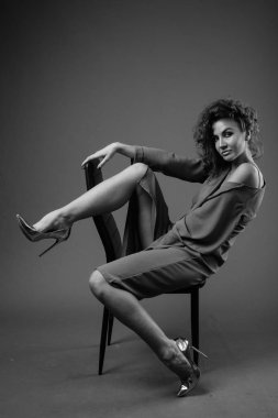 Studio shot of young beautiful woman with curly hair posing against gray background in black and white