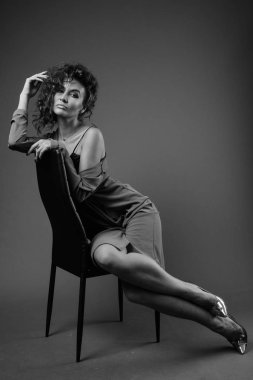 Studio shot of young beautiful woman with curly hair posing against gray background in black and white