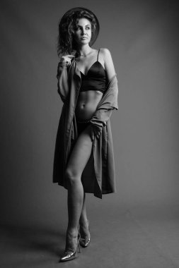 Studio shot of young beautiful woman with curly hair posing against gray background in black and white