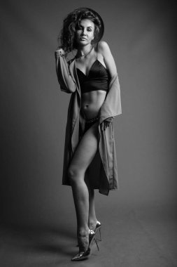 Studio shot of young beautiful woman with curly hair posing against gray background in black and white