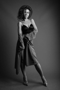 Studio shot of young beautiful woman with curly hair posing against gray background in black and white