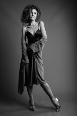 Studio shot of young beautiful woman with curly hair posing against gray background in black and white