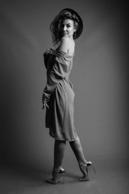 Studio shot of young beautiful woman with curly hair posing against gray background in black and white