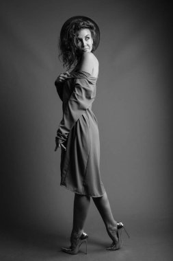 Studio shot of young beautiful woman with curly hair posing against gray background in black and white