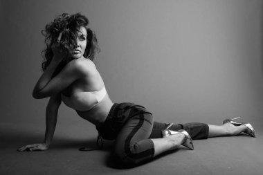 Studio shot of young beautiful woman with curly hair posing against gray background in black and white