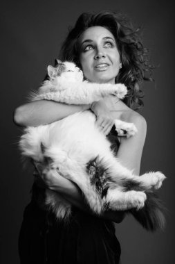 Studio shot of young beautiful woman with curly hair posing against gray background in black and white