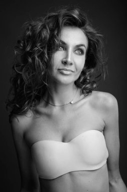 Studio shot of young beautiful woman with curly hair posing against gray background in black and white