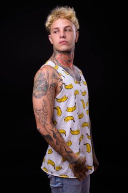 Studio shot of young handsome rebellious man with blond hair and tattoos against black background