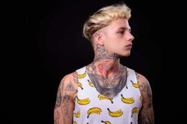 Studio shot of young handsome rebellious man with blond hair and tattoos against black background