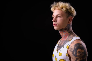 Studio shot of young handsome rebellious man with blond hair and tattoos against black background