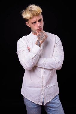 Studio shot of young handsome rebellious businessman with blond hair against black background