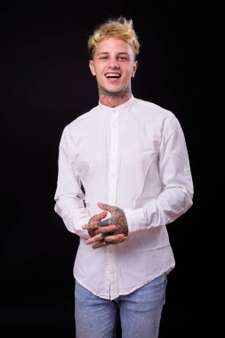 Studio shot of young handsome rebellious businessman with blond hair against black background