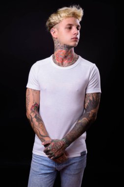 Studio shot of young handsome rebellious man with blond hair against black background