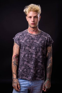 Studio shot of young handsome rebellious man with blond hair and tattoos against black background