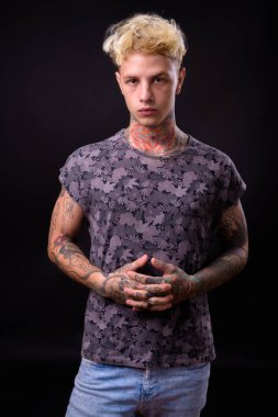 Studio shot of young handsome rebellious man with blond hair and tattoos against black background