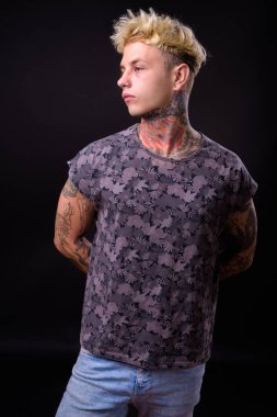 Studio shot of young handsome rebellious man with blond hair and tattoos against black background